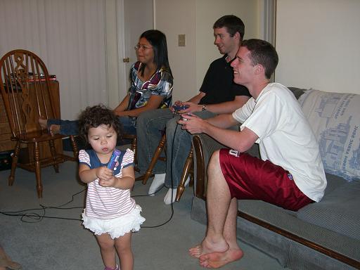 Abby, David, and Robert are playing video games while Hailey shakes a tube of quarters.